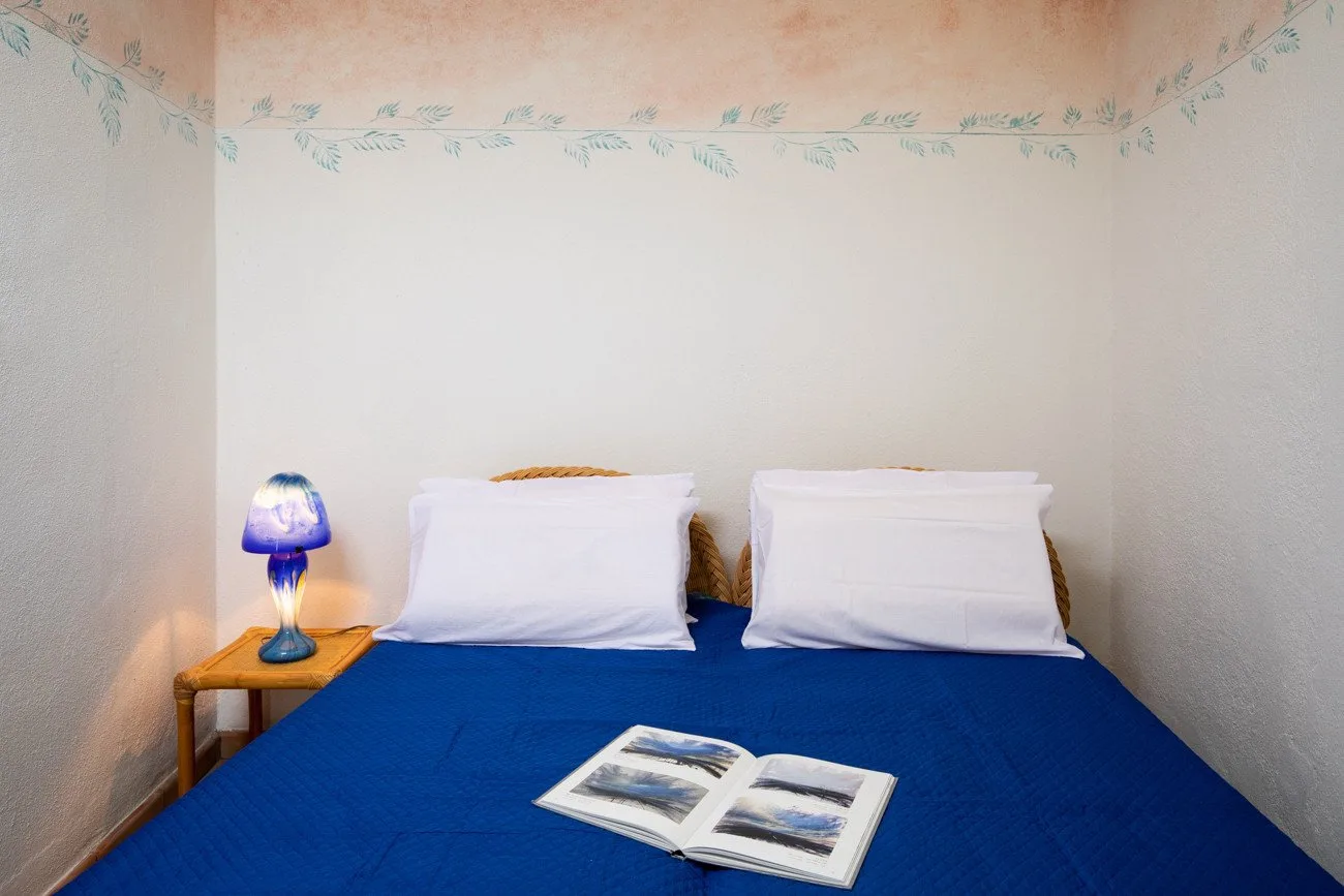 A bedroom with a blue-covered bed, two pillows, and an open book.