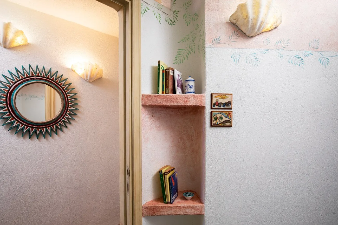 A pastel interior corner has a sunburst mirror, shell decorations, and built-in shelves.