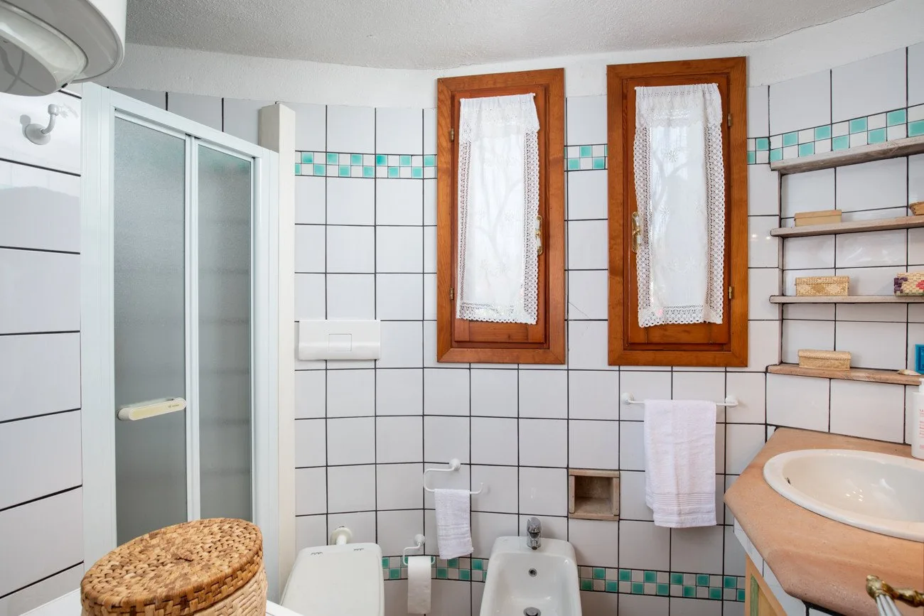 A tiled bathroom with a glass shower, a bathtub, and two curtained windows.