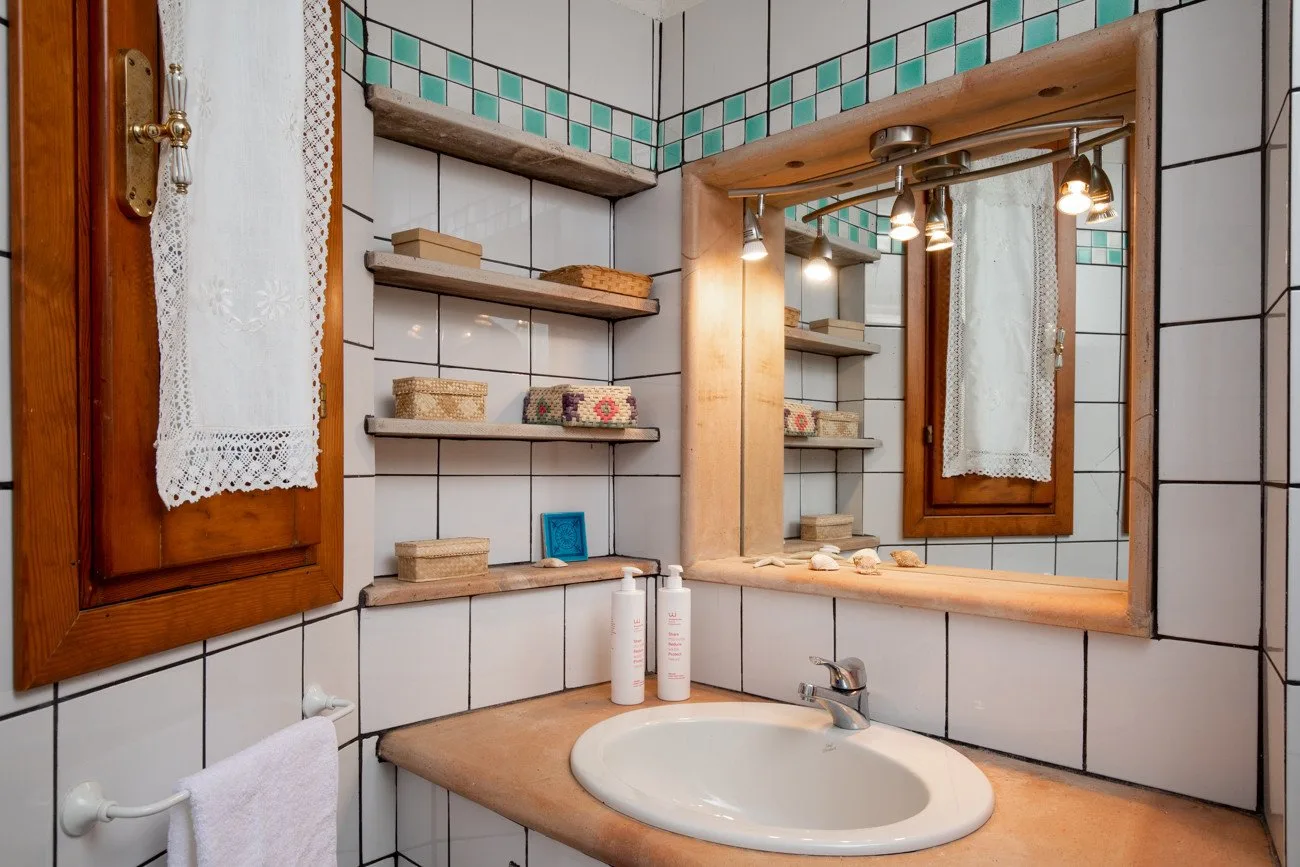 A tiled bathroom vanity with a sink, mirror, and wooden shelves.