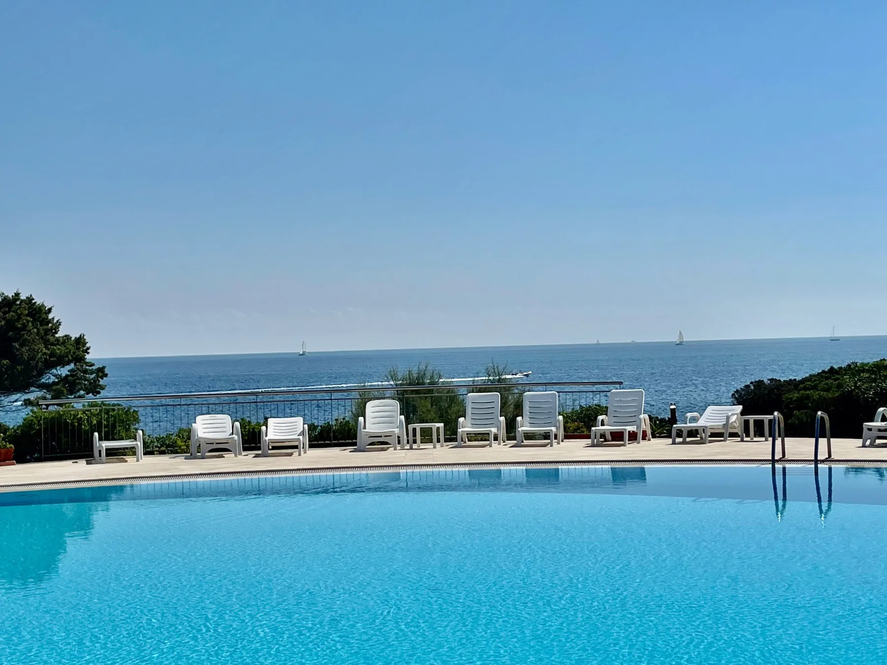 A swimming pool overlooks the sea, with lounge seating along the deck.