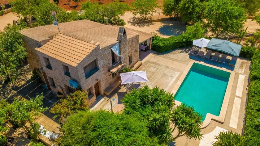 Vista aérea de una casa de piedra junto a una piscina turquesa y jardines.