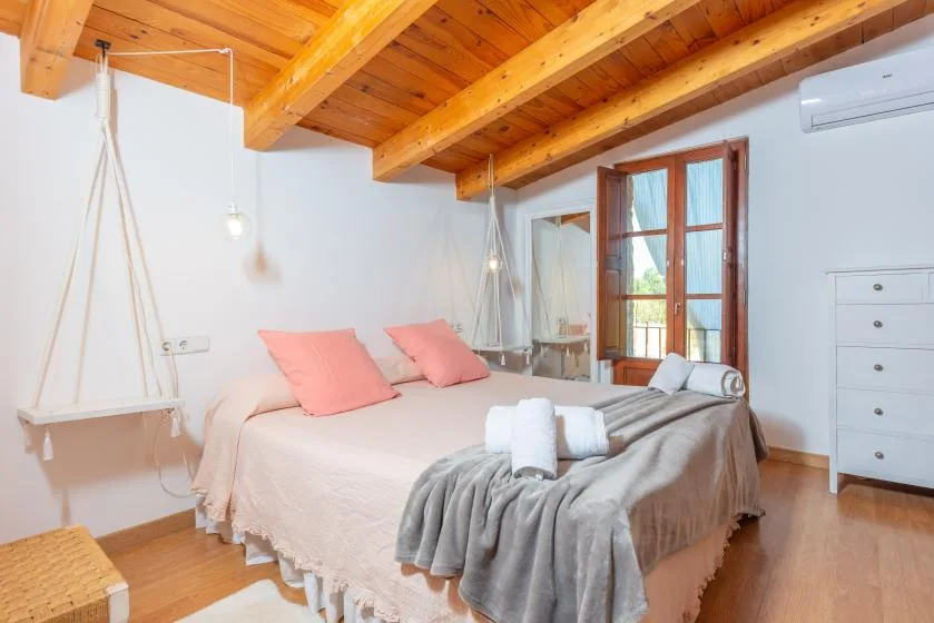 Un dormitorio con una cama, vigas de madera en el techo y puertas acristaladas que dan a un balcón.
