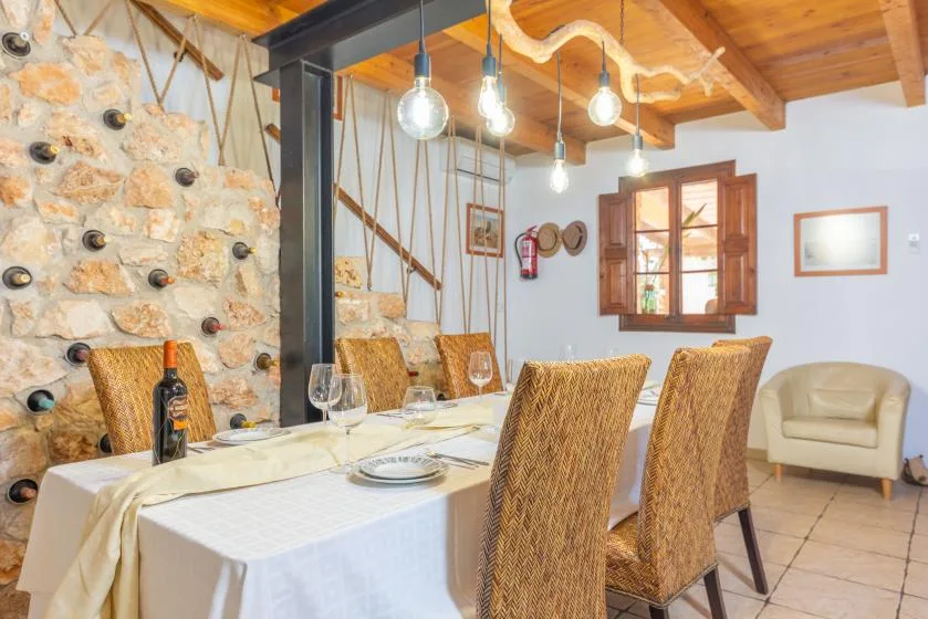 Comedor con una mesa puesta, sillas tejidas y una pared de piedra.