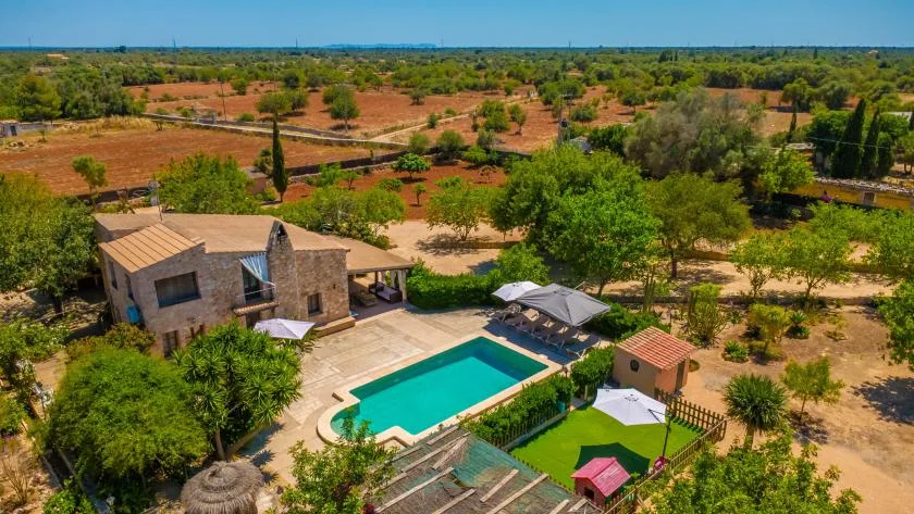 Vista aérea de una piscina junto a una casa en un paisaje seco con árboles.