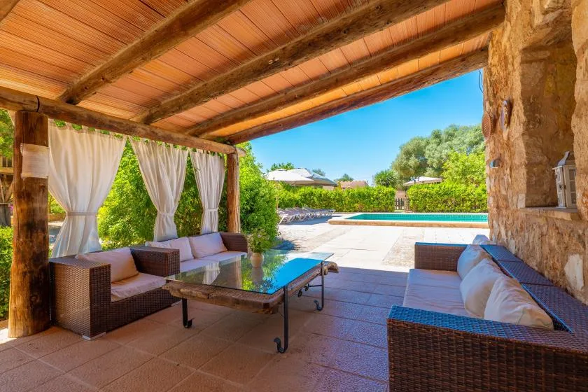 Un patio cubierto con asientos da a una piscina y un jardín.