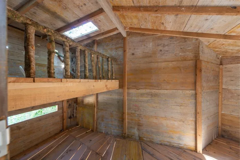 Un interior de madera con una plataforma elevada para dormir y una claraboya.
