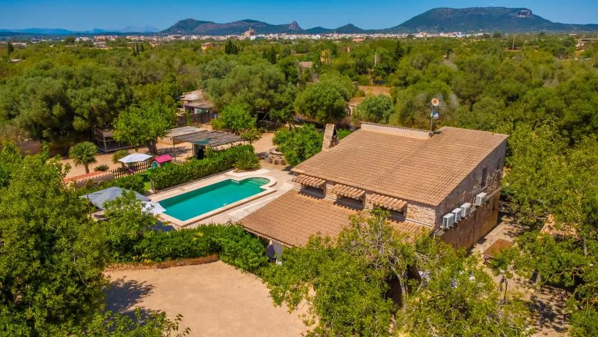 Vista aérea de una casa y una piscina rodeadas de vegetación, con colinas a lo lejos.