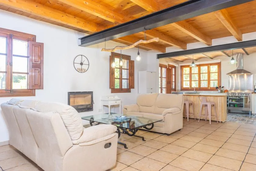 Una luminosa sala de estar se abre a la cocina, con asientos claros bajo un techo de madera.