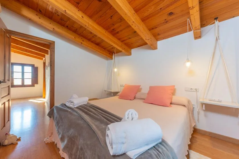 Un dormitorio con una cama bien arreglada bajo un techo con vigas de madera.