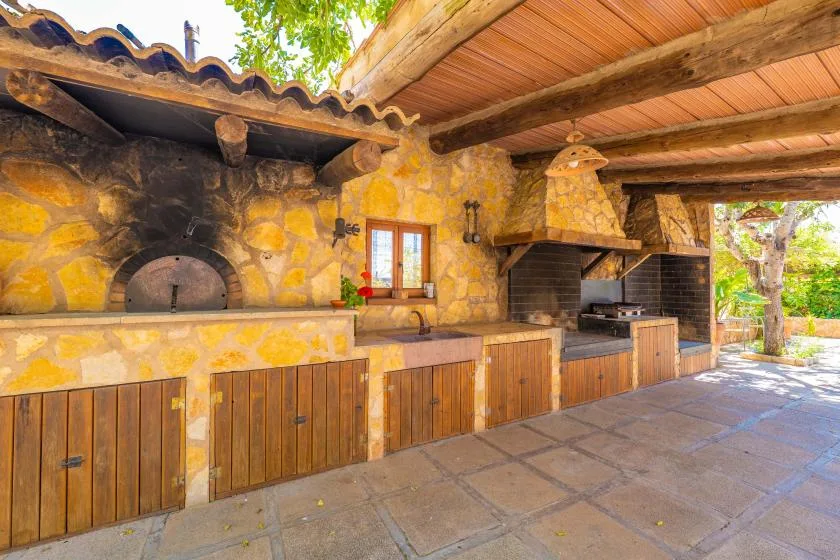 Una zona de cocina exterior de piedra con una encimera larga y parrillas empotradas.