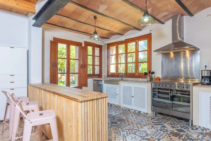 Una cocina luminosa con muebles de madera, suelo de baldosas estampadas y ventanas amplias.