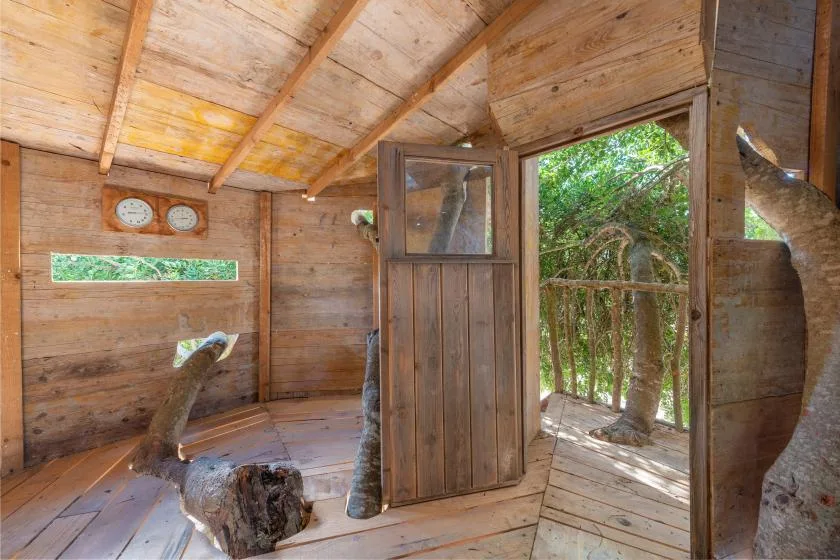 Un interior rústico de madera se abre a una terraza exterior frondosa por una puerta abierta.