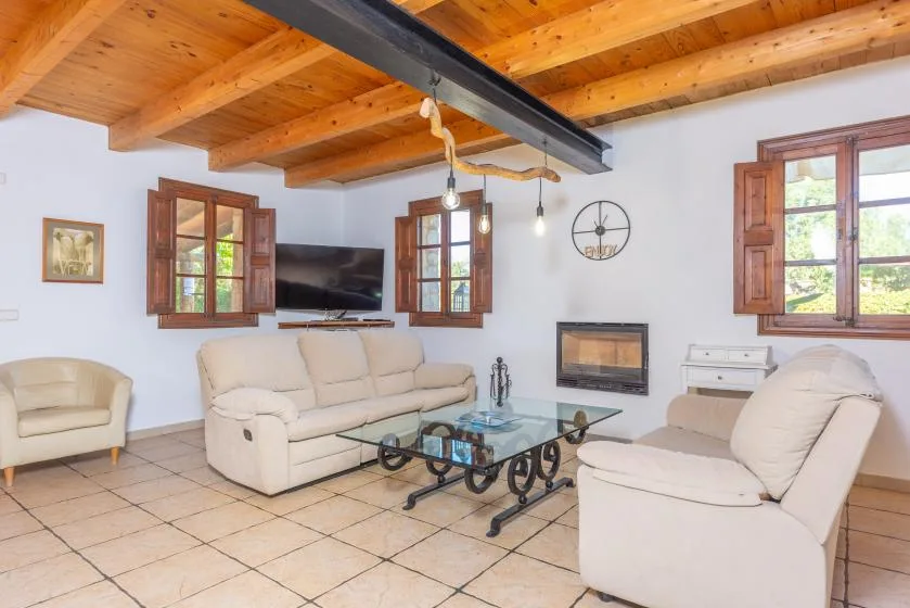 Una sala de estar con asientos claros, una mesa de centro de vidrio y vigas de madera en el techo.