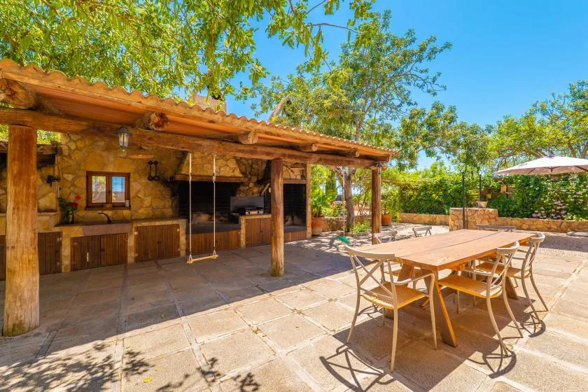 Una cocina exterior de piedra y una zona de comedor están bajo una pérgola de madera.
