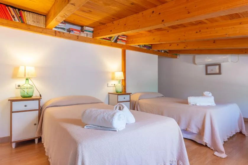 Un dormitorio con dos camas, mesitas de noche y un altillo de madera encima.