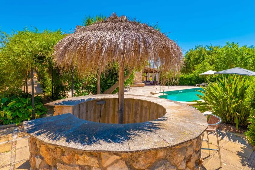 Una palapa de techo de paja cubre una barra circular de piedra junto a una piscina.