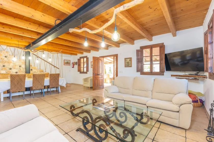 Una luminosa sala de estar y comedor con vigas de madera a la vista y una mesa de centro de vidrio.