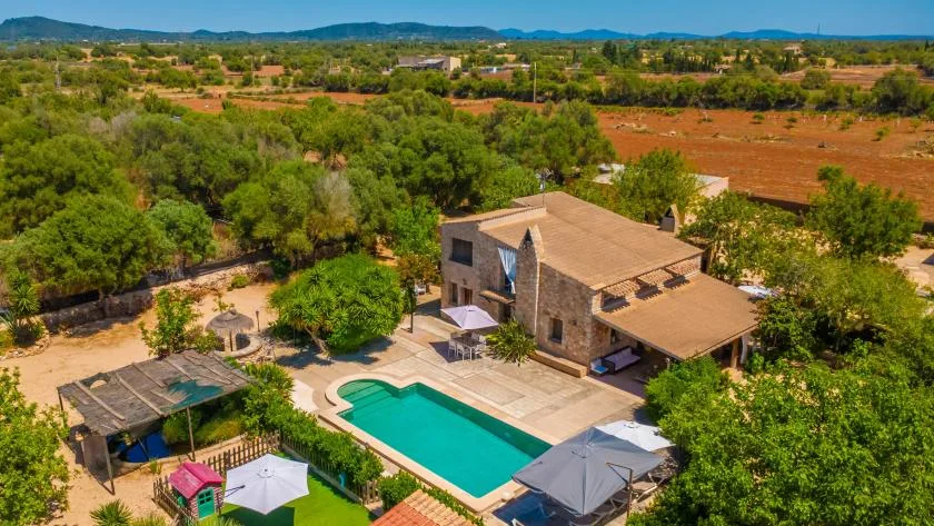 Vista aérea de una casa con piscina entre árboles verdes y campos abiertos.