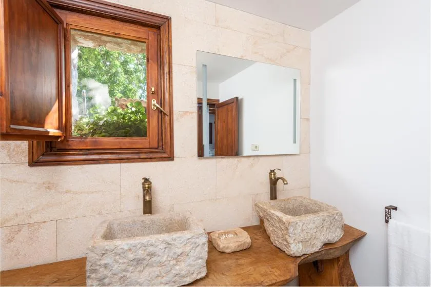 Un lavabo de baño con dos lavabos de piedra sobre una encimera y bajo un espejo.