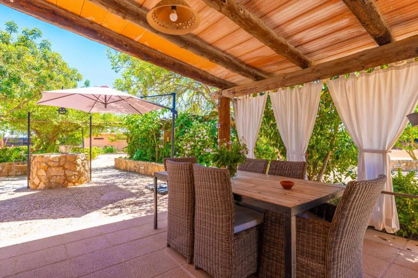 Un comedor exterior cubierto tiene una mesa y asientos junto a la vegetación del jardín.