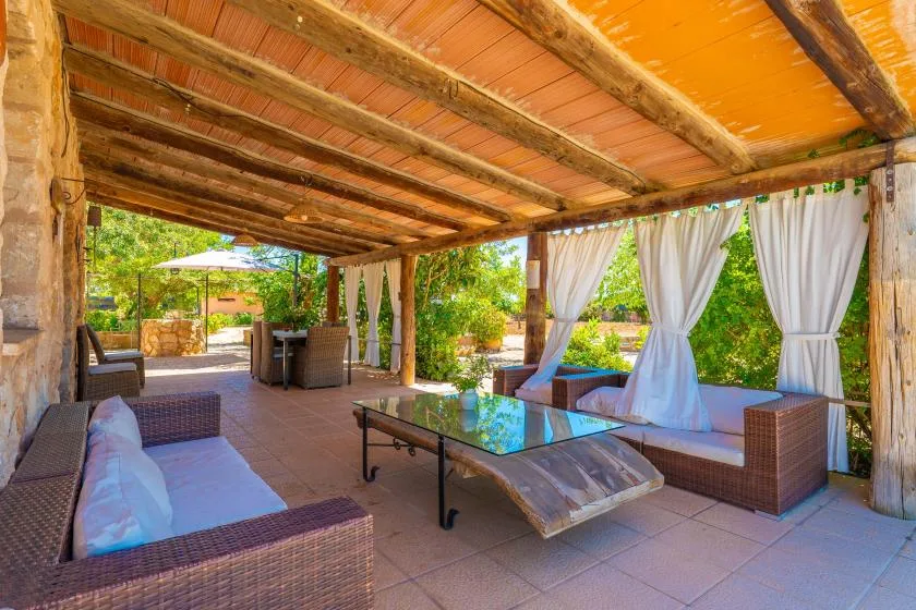 Una zona de estar exterior cubierta con cortinas y una mesa de centro de cristal.