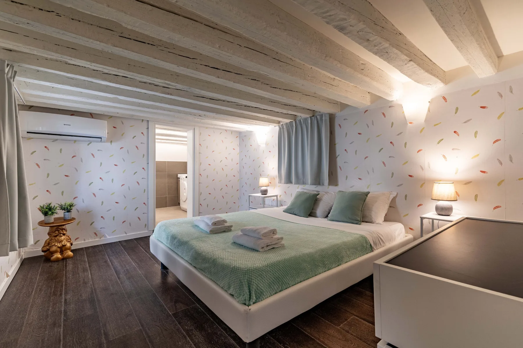 Un dormitorio con una cama bien tendida bajo vigas expuestas en el techo.