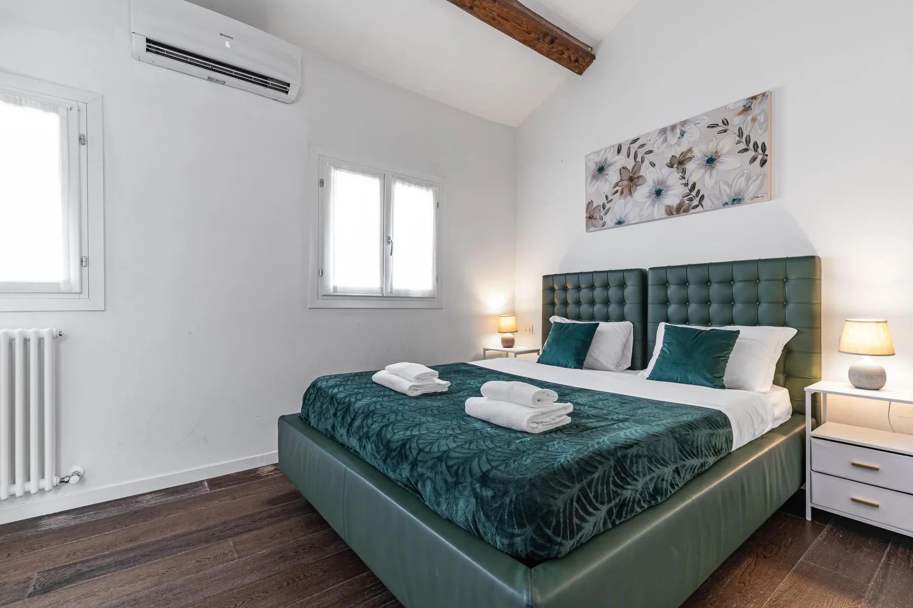 Un dormitorio con una cama grande, ropa de cama verde azulado y un cabecero acolchado.