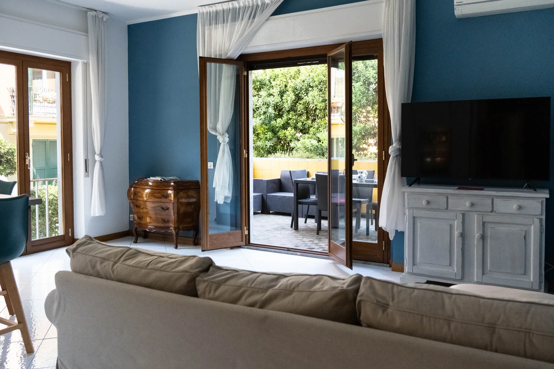 Una sala de estar con paredes azules, asientos y puertas abiertas a un patio.