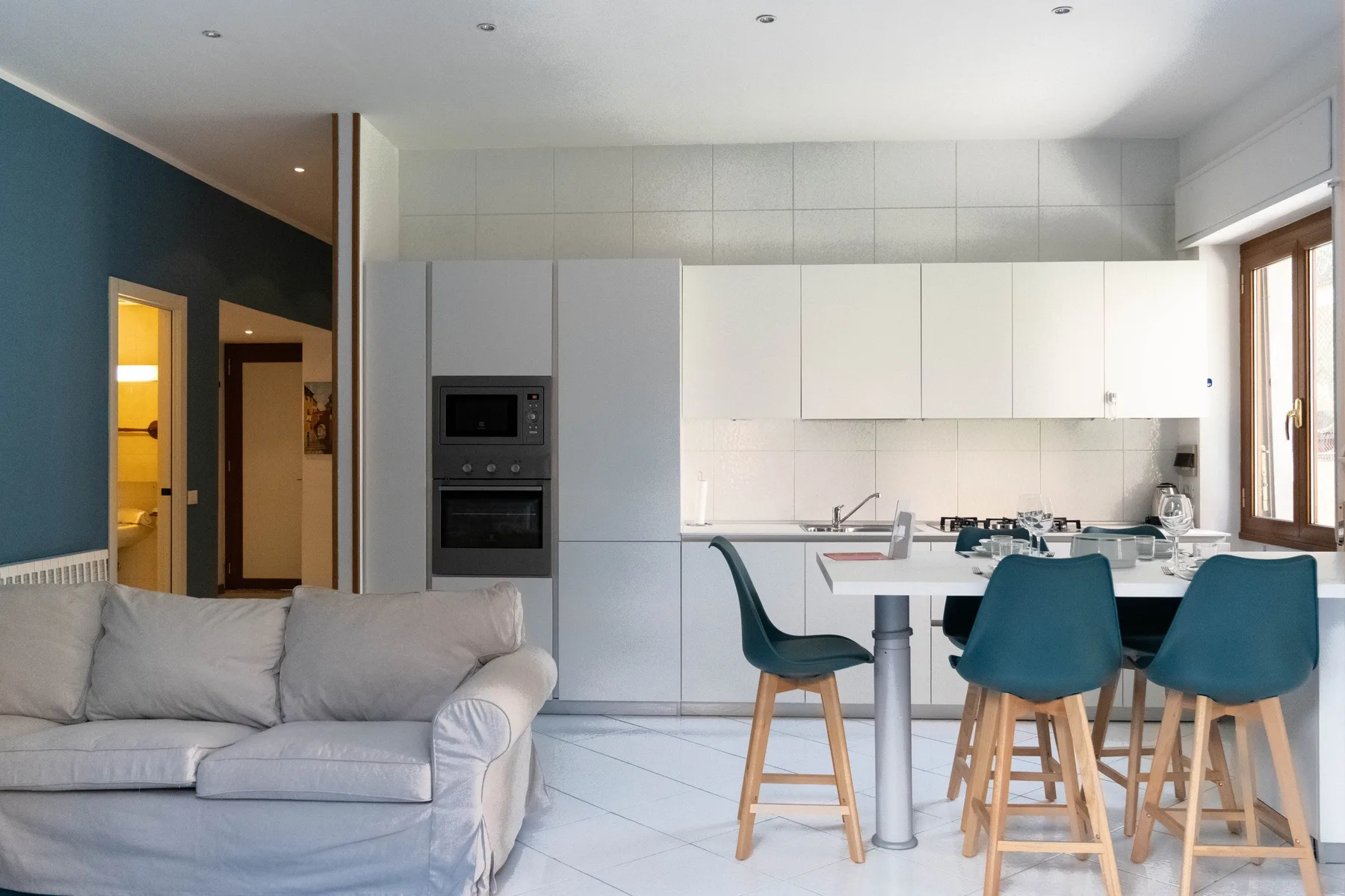 Una sala de estar se abre a una cocina y una mesa de comedor con asientos color turquesa.