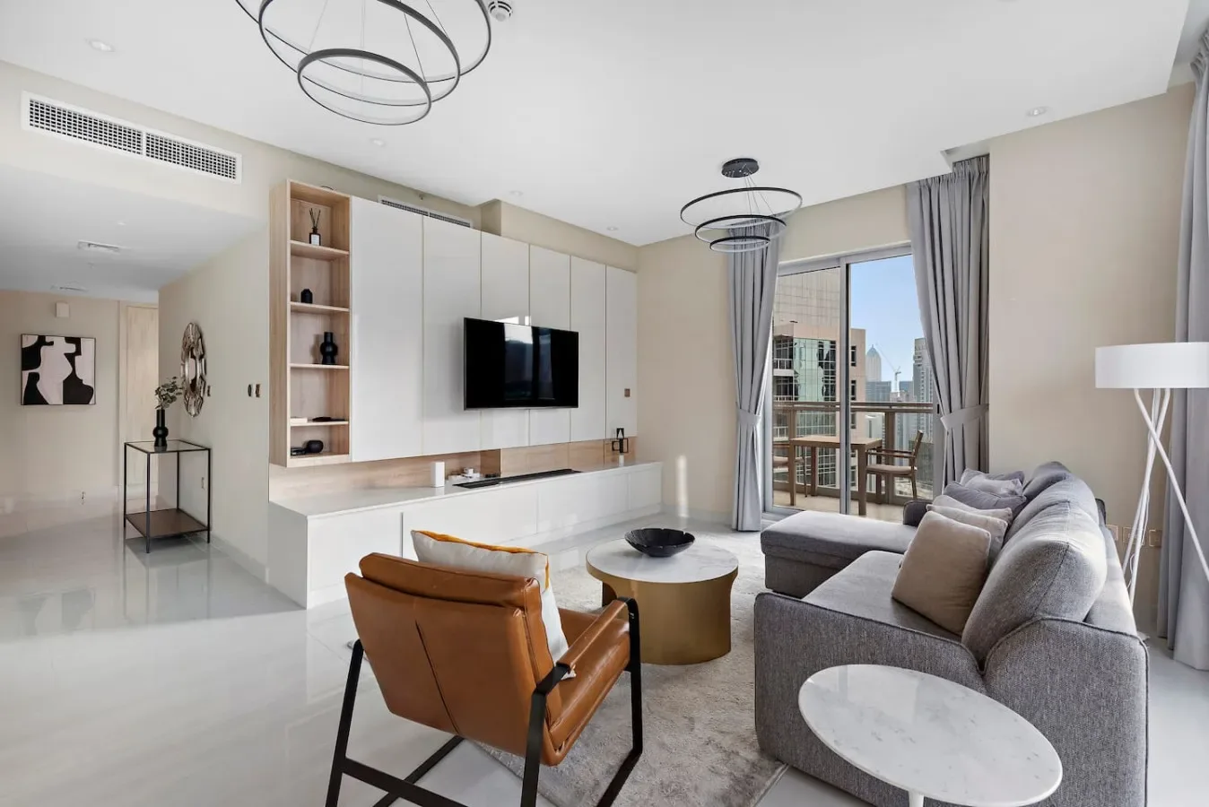 Una sala luminosa con asientos, un televisor y grandes ventanas con vista a un balcón.