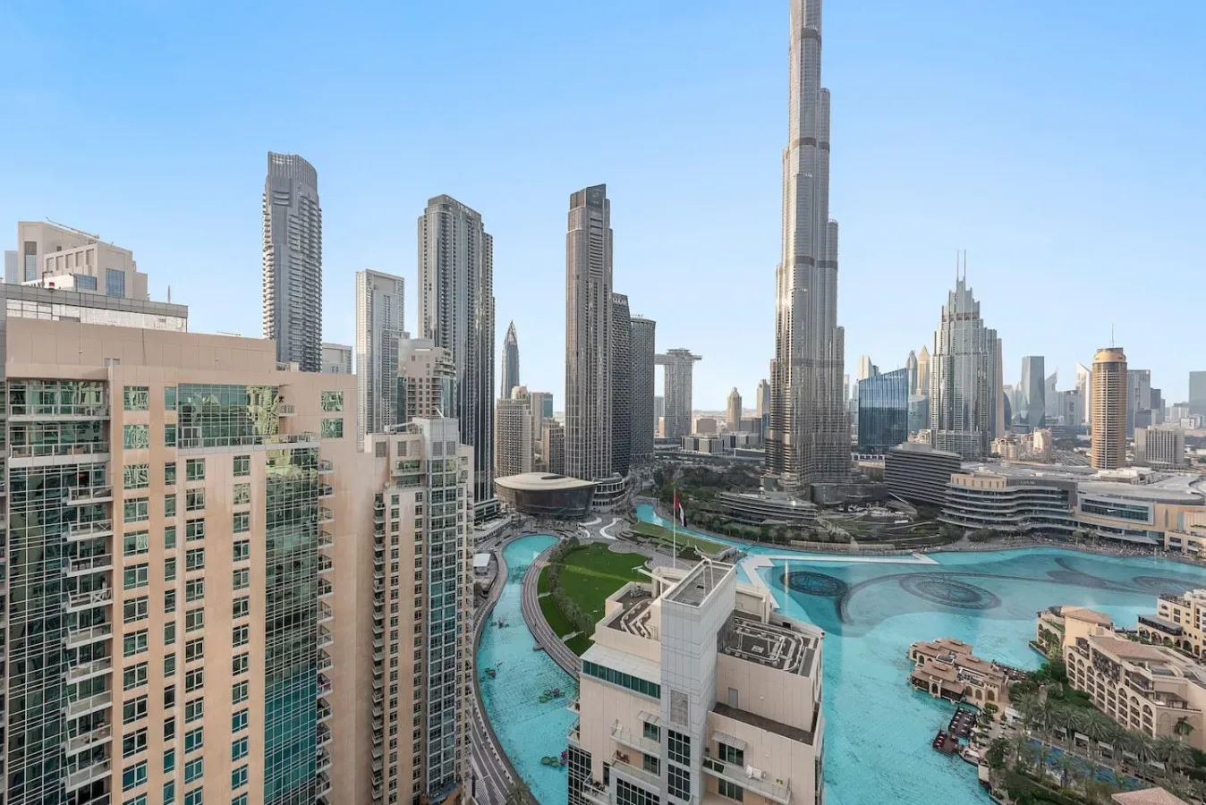 A city skyline rises above a turquoise pool and landscaped grounds.