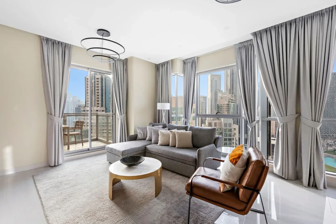 Una sala luminosa con sofá seccional gris, sillón y vistas a la ciudad.