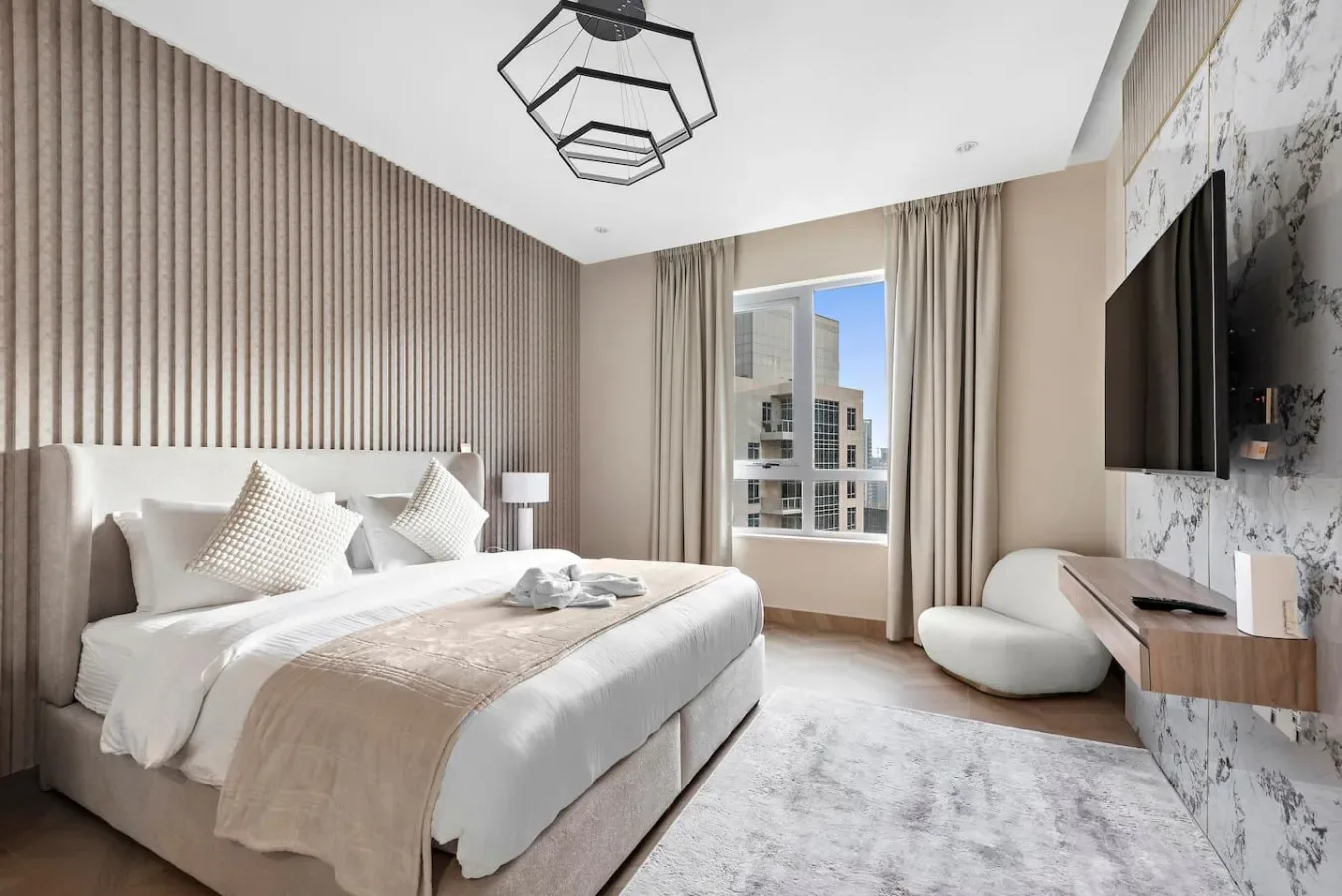Dormitorio con una cama bien tendida, una ventana alta y un televisor montado en la pared.