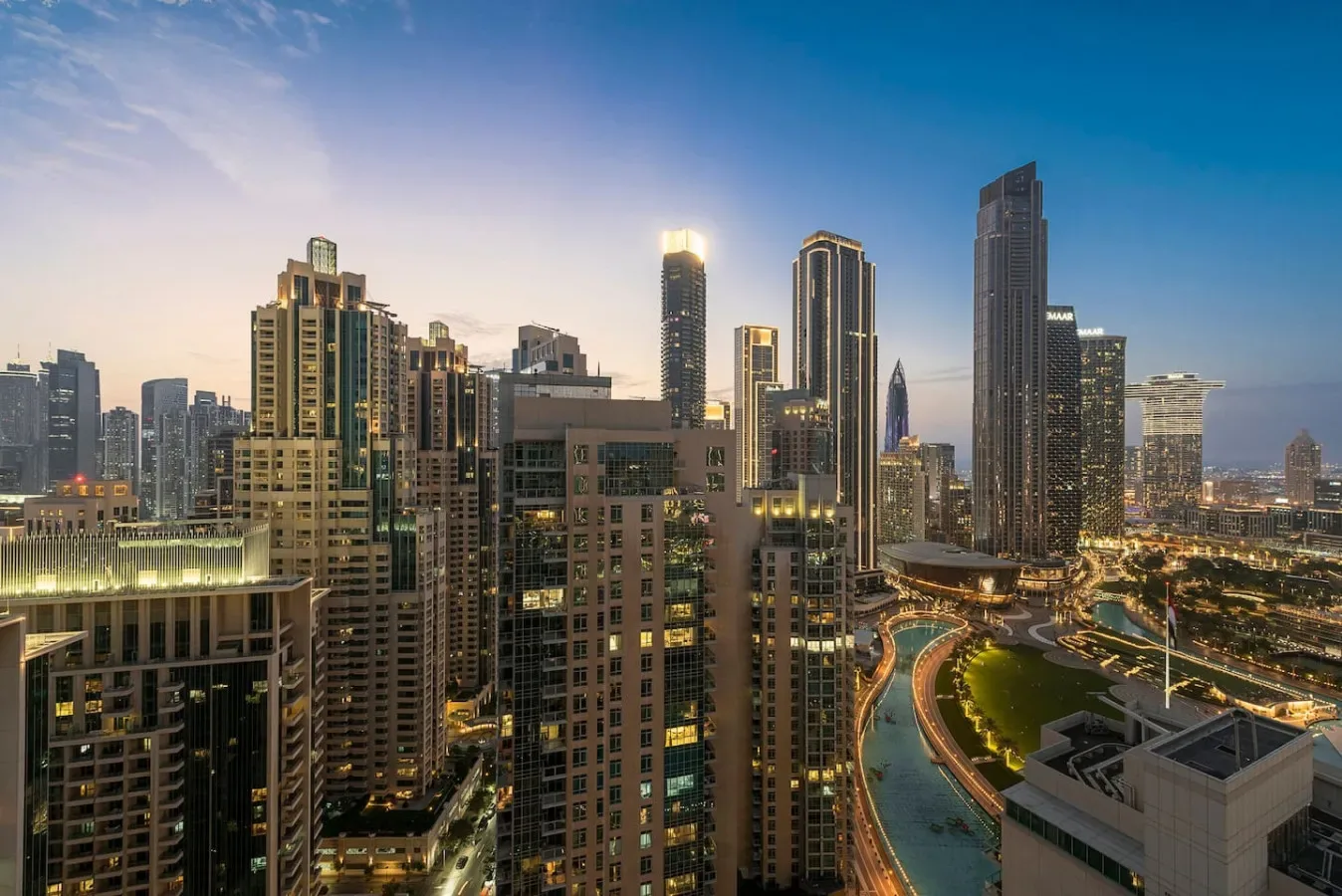 A city skyline at dusk, with illuminated towers and curving roads.