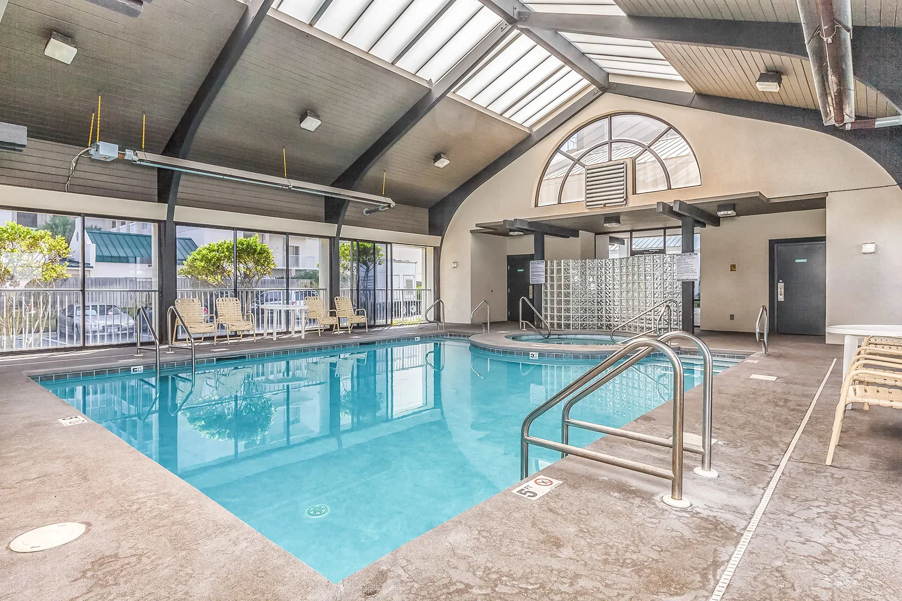 An indoor swimming pool with large windows and metal handrails.