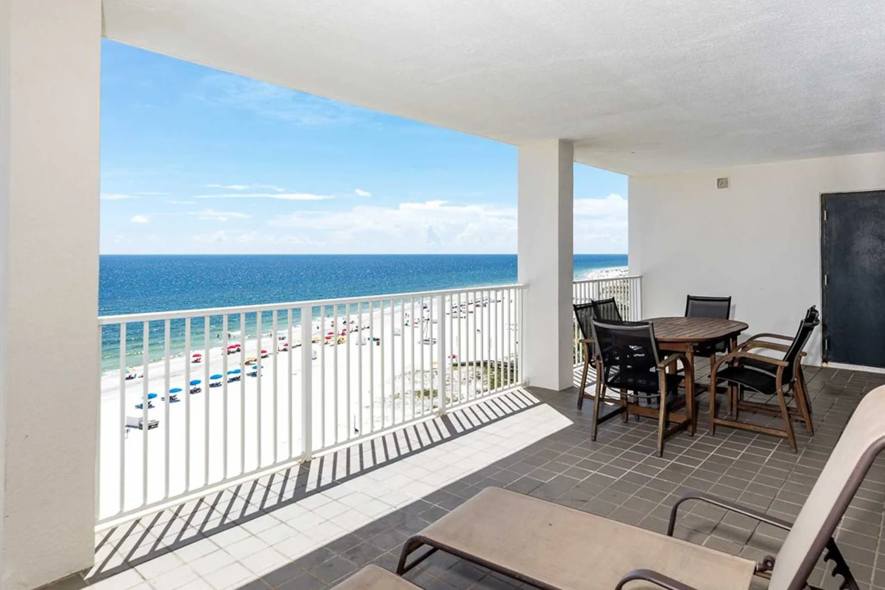 A covered balcony overlooks the ocean, with a table and seating nearby.