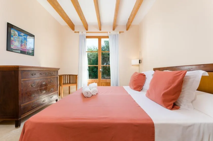 Dormitorio con una colcha coral, una cómoda de madera y puertas de cristal.