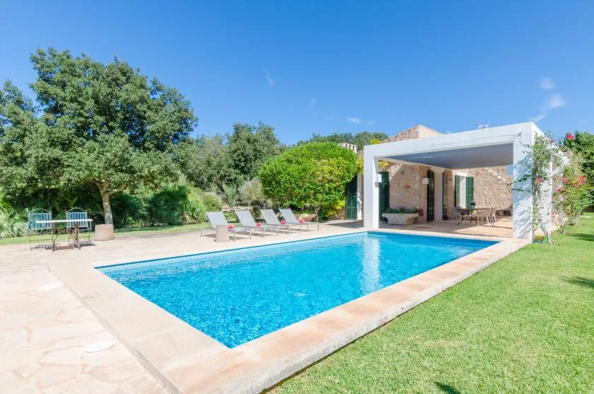 An outdoor swimming pool beside a covered patio and green lawn.
