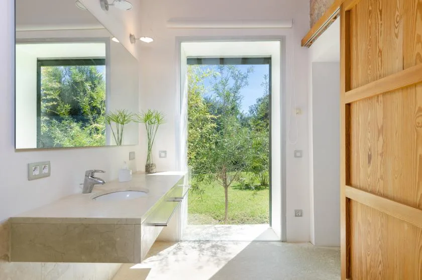 Un baño luminoso con lavabo y una ventana grande con vistas a la vegetación.