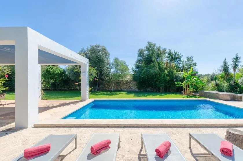 Piscina al aire libre junto a una pérgola blanca, con tumbonas en el patio.