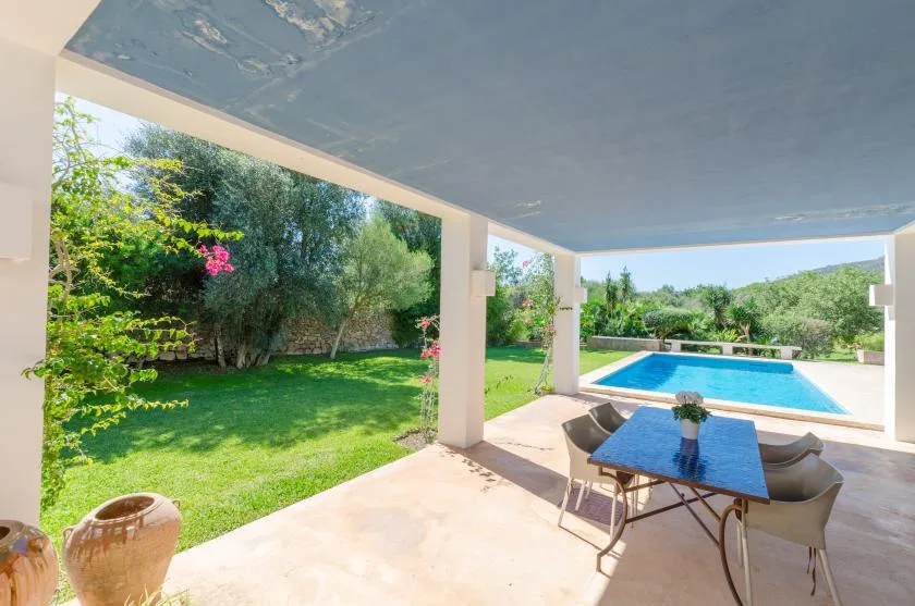 Un patio cubierto con una mesa de comedor da a un césped y una piscina.