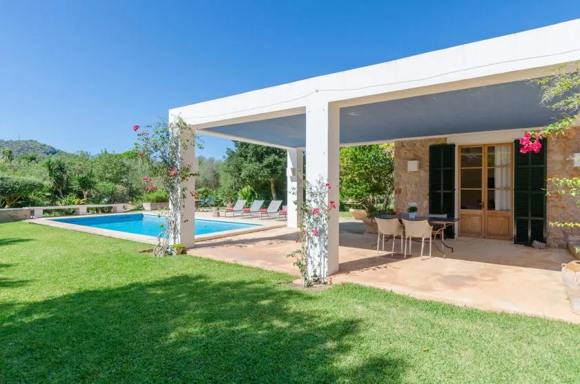Un patio cubierto con asientos al aire libre da a una piscina y un césped.