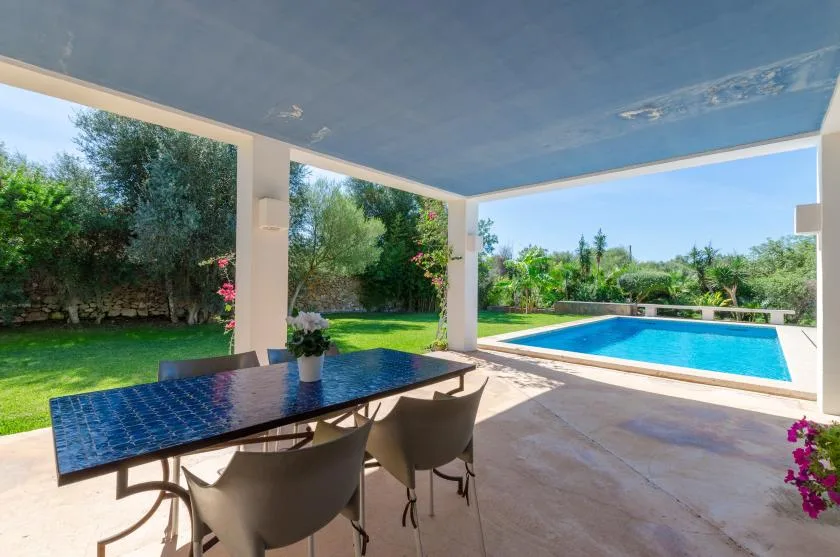 Una zona de comedor exterior cubierta da a una piscina y un jardín ajardinado.