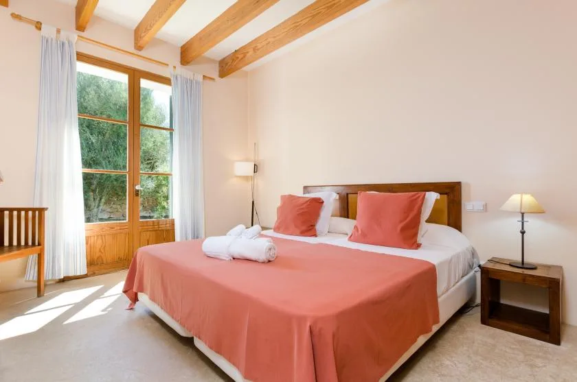 Un dormitorio con una cama vestida de coral junto a una ventana alta.