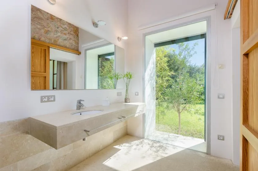 Un baño luminoso con un amplio tocador y una puerta de vidrio grande hacia la vegetación.