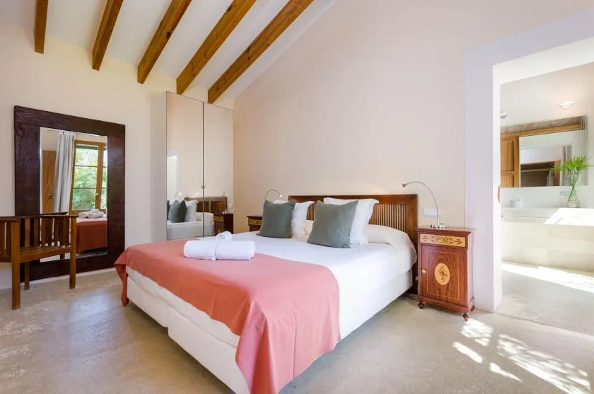 Un dormitorio luminoso con una cama vestida de blanco y una manta coral.