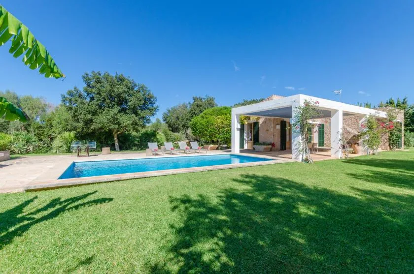 A swimming pool beside a lawn and an open-sided pavilion.