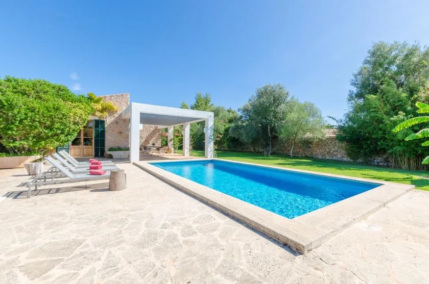 A swimming pool beside a paved patio, with seating and a white pergola.