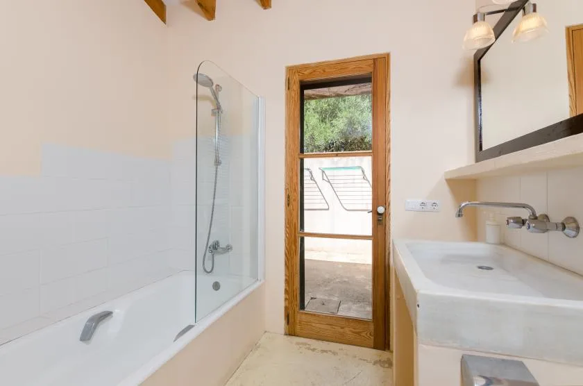 Un baño luminoso con bañera, ducha y puerta de vidrio con marco de madera.